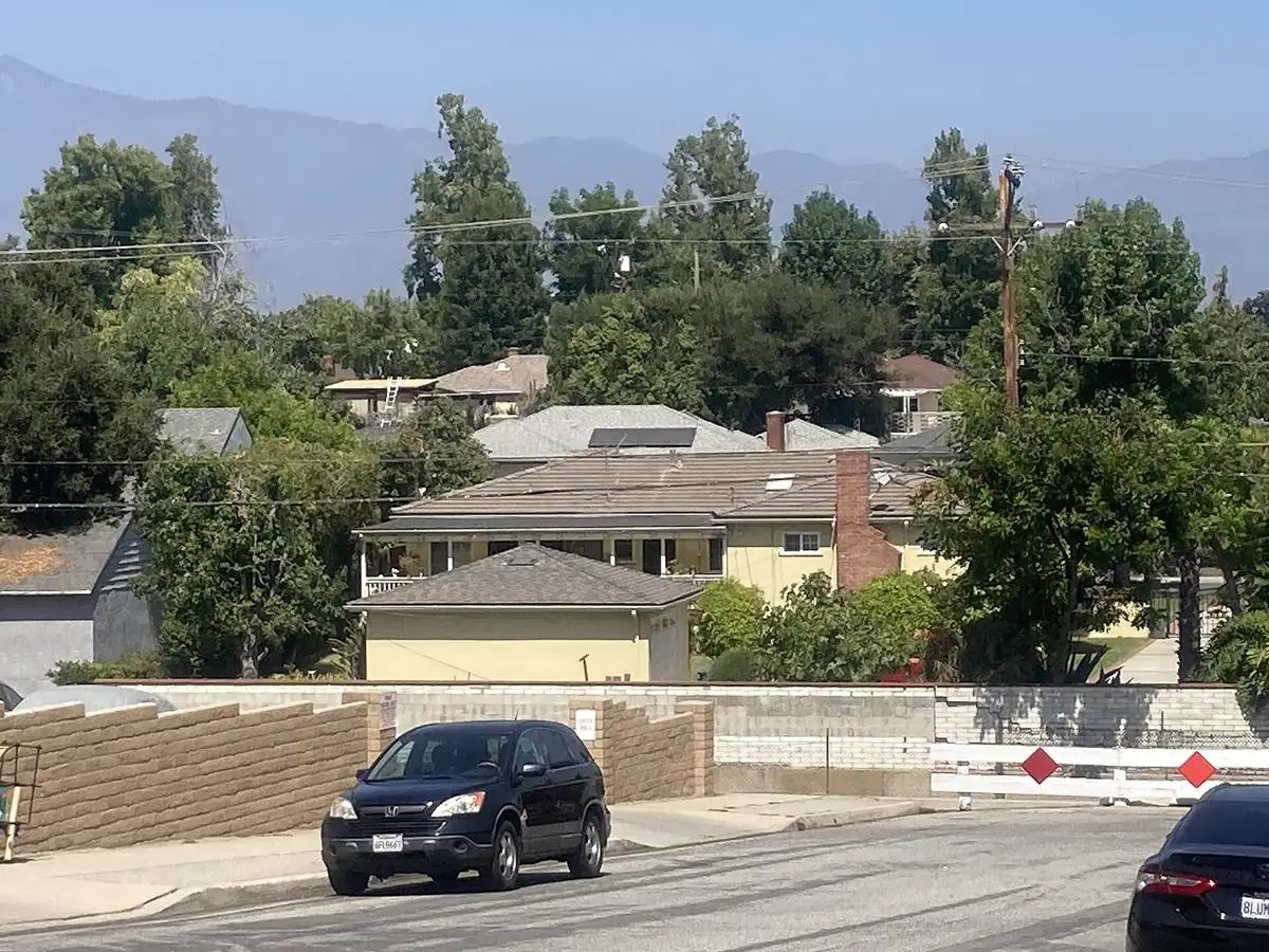 Houses among tall trees on a San Gabriel Valley street, with the San Gabriel Mountains faint in the haze